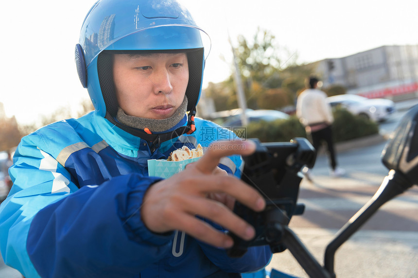 外卖员吃着肉夹馍查看手机订单图片