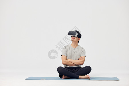 坐在瑜伽垫上操作vr设备的男性高清图片