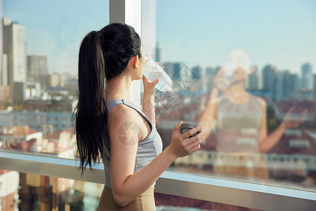 健身后站在窗边喝水的女性高清图片