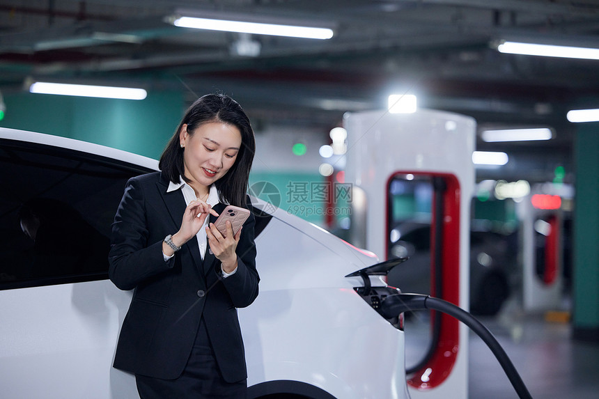 新能源汽车旁使用手机的白领女性图片