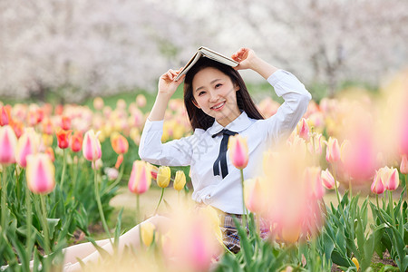 坐在郁金香花海里看书的制服女性高清图片