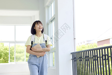 手捧书本的女大学生走在校园里图片