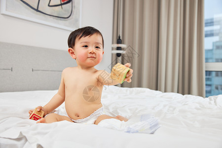 婴儿宝宝坐在床上手拿玩具背景图片
