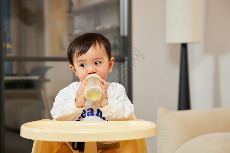 坐在宝宝椅上手拿奶瓶的小宝宝高清图片