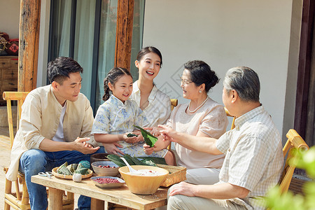 坐在粽子叶上端午节在院子里包粽子的一家人背景