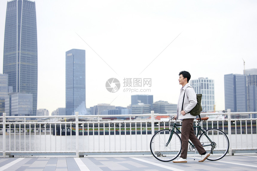 年轻男性江边推着自行车行走图片