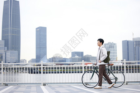 行走出游年轻男性江边推着自行车行走背景