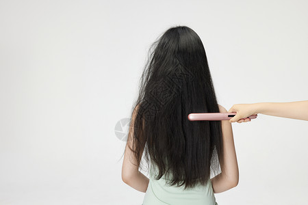 年轻女性使用夹板拉直头发背影背景