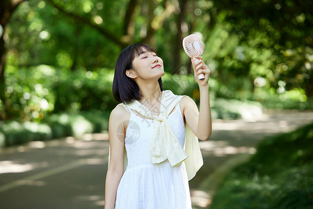 手拿小风扇户外手拿便携风扇吹风的少女背景