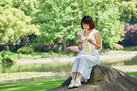 女生夏日坐在河边石头上看书背景