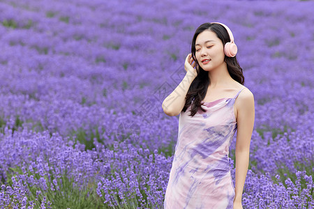 夏日连衣裙美女戴着耳机听音乐走在薰衣草花田的女性背景