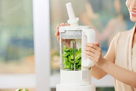 女子使用榨汁机榨绿色食品特写高清图片