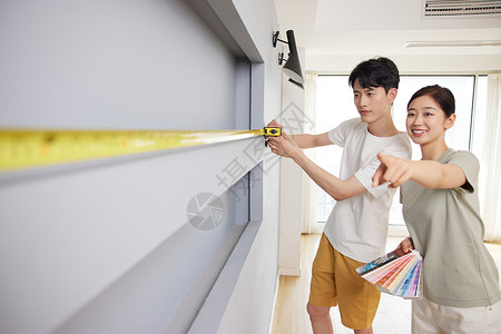 新婚夫妻测量新房墙面长度高清图片