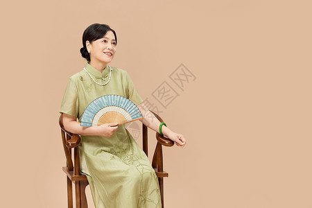 穿旗袍的女性手拿扇子坐在椅子上背景图片