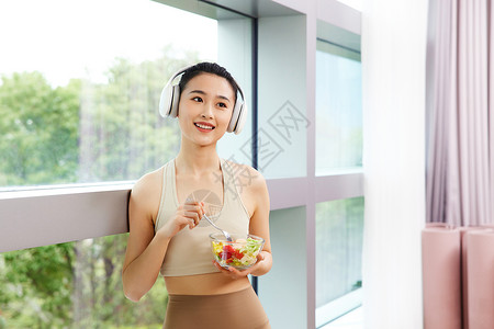 女人零食休息时听音乐吃色拉的运动女生背景