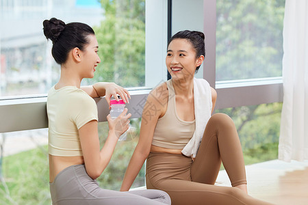 女性瑜伽健身手捧水杯休息聊天说笑的两位运动女生背景