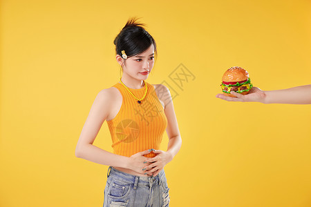 看着汉堡捂肚子的时尚女性图片