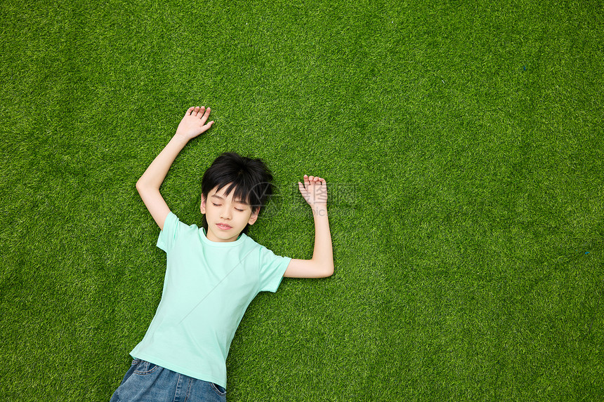 小男孩躺在草坪上闭眼休息图片