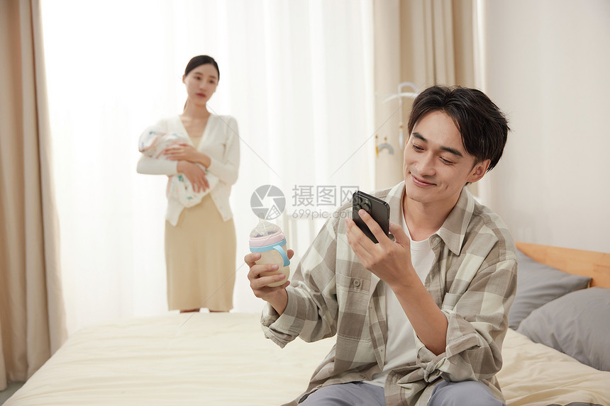 抱孩子的母亲和拿着奶瓶玩手机的父亲图片