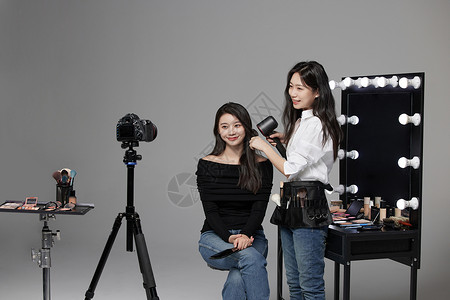 美女拿相机直播化妆师使用吹风机给模特做造型背景