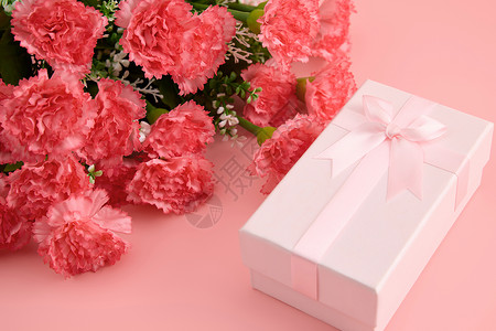 浅红色蝴蝶结一大束娇艳欲滴的红色康乃馨和粉色蝴蝶结礼物盒背景