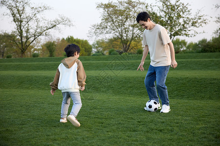 运动亲子父子户外草地上踢足球背景