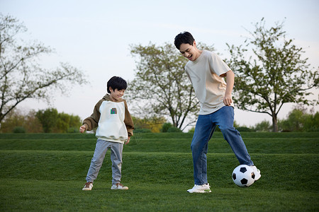 传球父亲和儿子在户外草地上踢足球背景