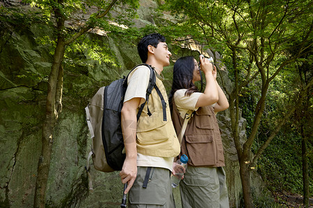 背包旅行的美女一对情侣拿着相机在拍山上景色背景