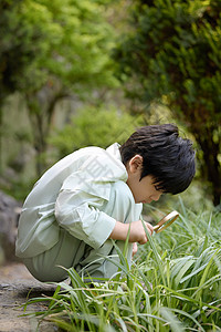 小男孩拿着放大镜蹲在地上观察植物背景