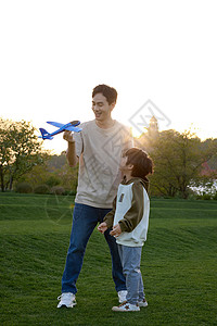 做飞机孩子草坪上教儿子玩飞机模型的爸爸背景