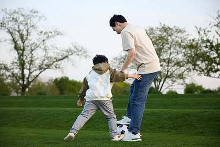 炸酱草和爸爸在草坪上玩足球的小男孩背景