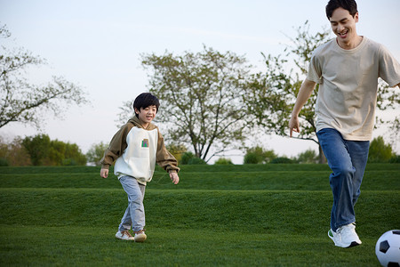 父子奔跑和爸爸在草坪上玩足球的小男孩背景