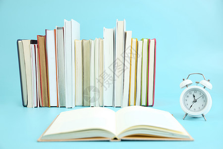 一叠彩色的书籍边有一本翻开的书与闹钟高清图片