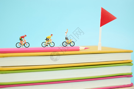 彩色旗帜飘带在一叠彩色书本上骑行冲向终点的微距小人背景