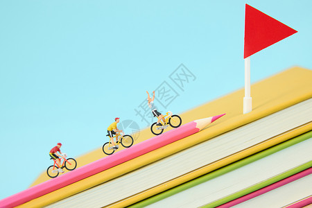 彩色旗帜飘带在一叠彩色书本上骑行冲向终点的微距小人背景