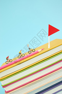 在一叠彩色书本上骑行冲向终点的微距小人高清图片