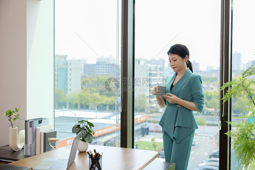 商务女性拿着咖啡站在办公室窗边图片