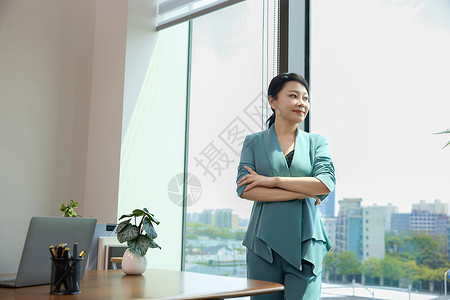 女白领双臂交叉站在办公室窗边高清图片