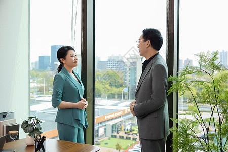 一个男白领和一位女白领站在办公室窗边讨论业务高清图片