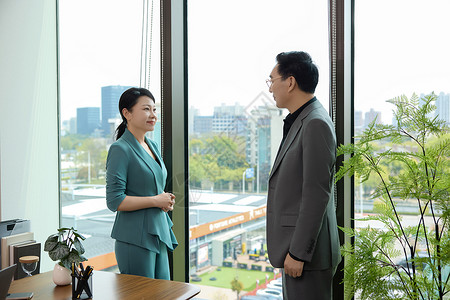 一个男白领和一位女白领站在办公室窗边讨论业务高清图片