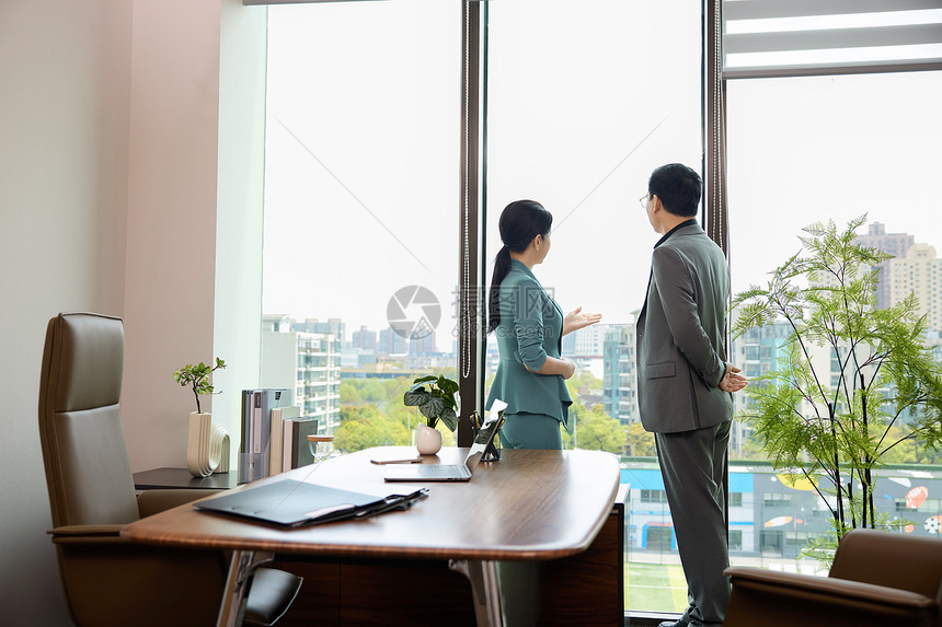 一个男白领和一位女白领站在办公室窗边讨论业务图片