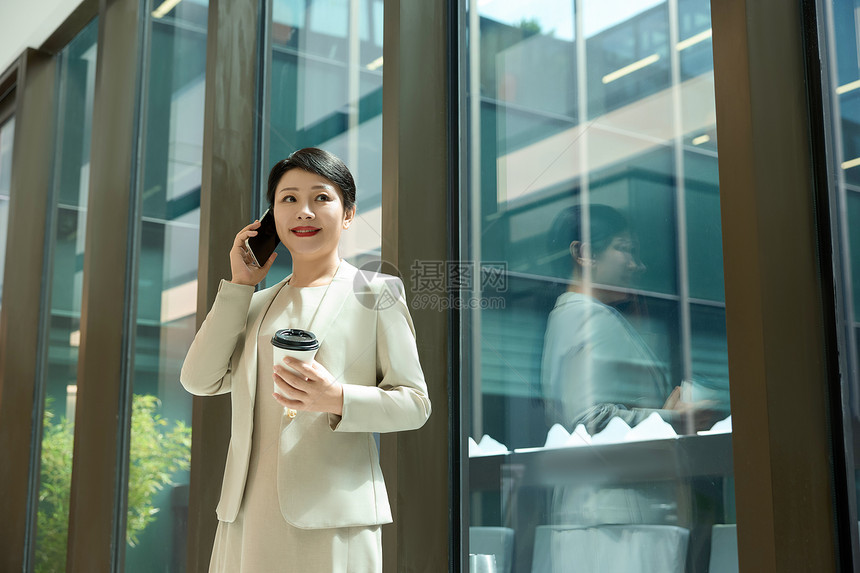 女白领在公司走廊拿着咖啡打电话图片