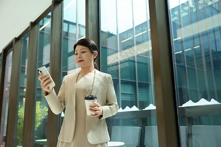 公司咖啡女白领在公司走廊拿着咖啡对手机笑背景