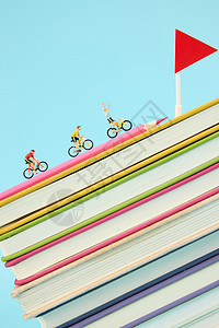 彩色旗帜飘带彩色书籍上骑行的创意微距小人背景