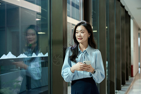 商务女性手机公司走廊拿着手机看窗外的女职员背景