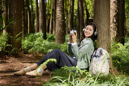 坐在森林里带耳机听歌放松的女孩高清图片