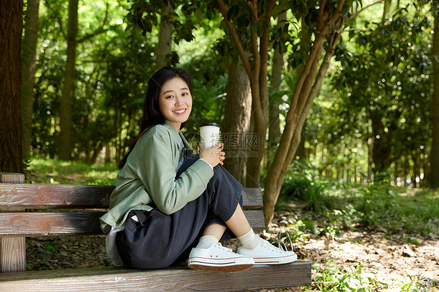 拿着咖啡杯坐在公园长椅上的美女图片