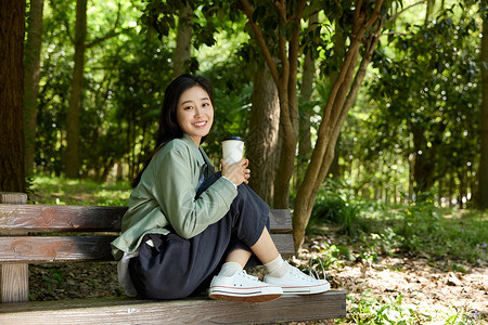 美女春天拿着咖啡杯坐在公园长椅上的美女背景