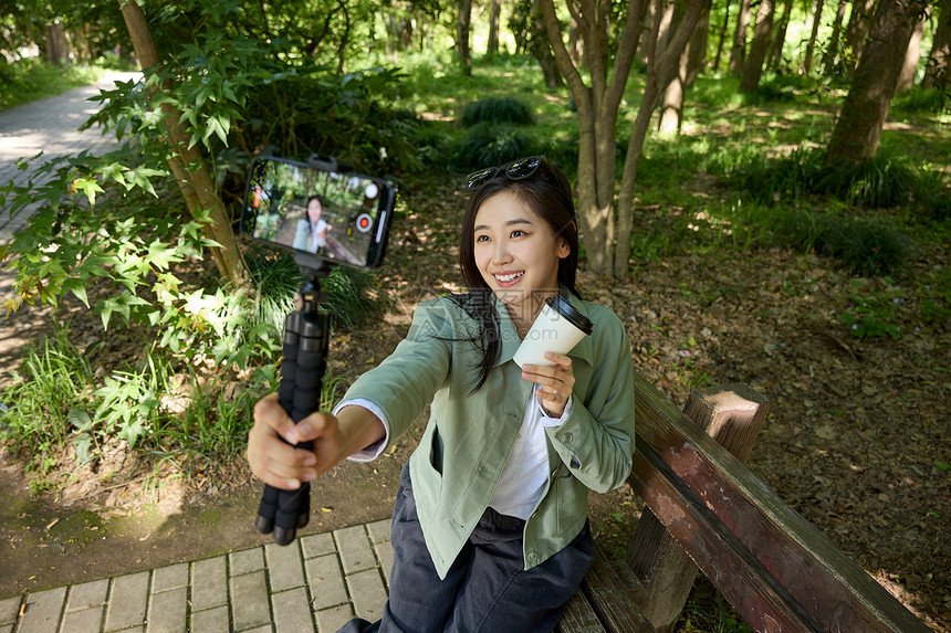 公园里拿着咖啡杯用相机自拍的美女图片