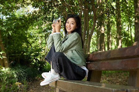 拍照翻译坐在公园长椅上拿着相机拍照的美女背景